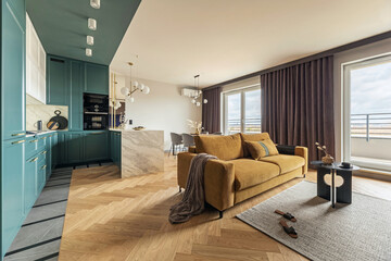 Creative and modern vintage open space interior design with yellow sofa and turqoise kithen with a marble island. Grey carpet on the herringbone parquet with coffe table, brown curtain in windows. 
