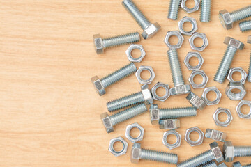 Closeup minimal style of beautiful and clean group of many metal steel silver chrome bolts and nuts scatted on wooden background and texture with copy space for text. Minimal hardware concept.