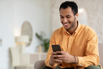 Happy Arab man using cellphone wearing wireless headphones