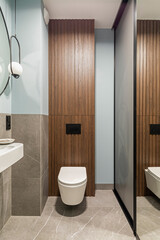 Modern bright bathroom with white toilet seat on wooden lamela wall. Mirror on grey wall.