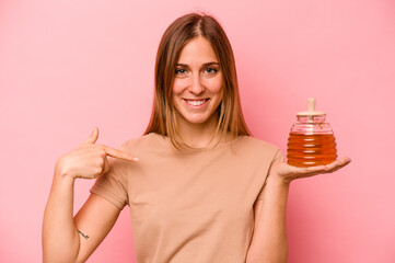Fototapeta premium Young caucasian woman holding honey isolated on pink background person pointing by hand to a shirt copy space, proud and confident