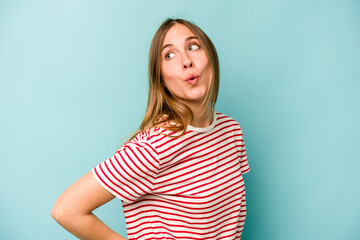 Obraz premium Young caucasian woman isolated on blue background looks aside smiling, cheerful and pleasant.