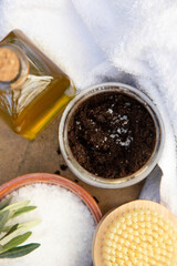 A jar of handmade coffee scrub, sea salt, body brush with olive oil are on a brick background. View from the top point.