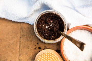 A jar of handmade coffee scrub, sea salt and a body brush with a white bath towel are on a brick background. View from the top point. Free space for text.