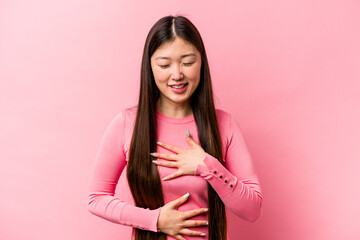 Young Chinese woman isolated on pink background laughs happily and has fun keeping hands on stomach.