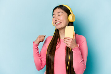 Young asian woman listening to music isolated on blue background