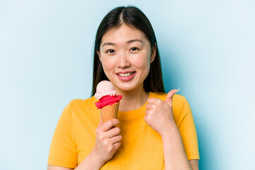 Young asian woman eating an ice cream isolated on blue background