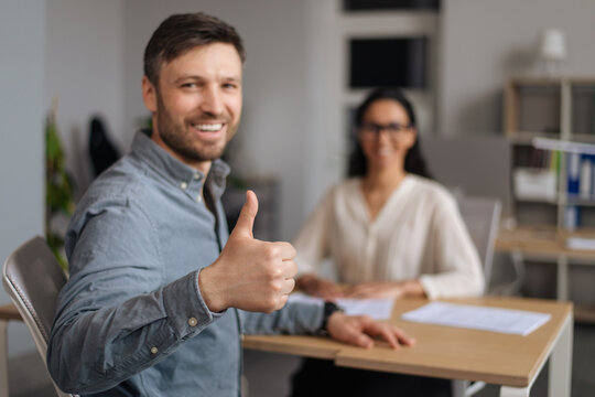 Joyful Caucasian guy showing thumb up during successful job interview with HR manager, being accepted to open vacancy