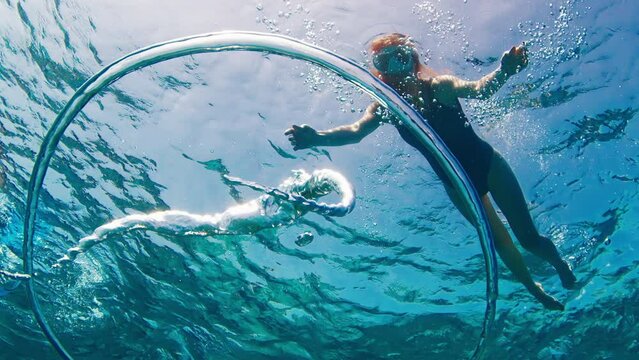 Woman swims underwater and watches ring bubble moving towards the surface