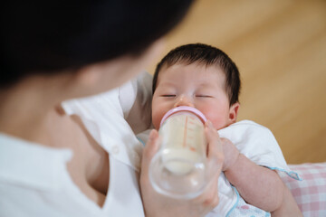 cropped view of asian mom looking at baby drinking breast milk from bottle. high angle view of lovely newborn having milk with eyes close. - Powered by Adobe