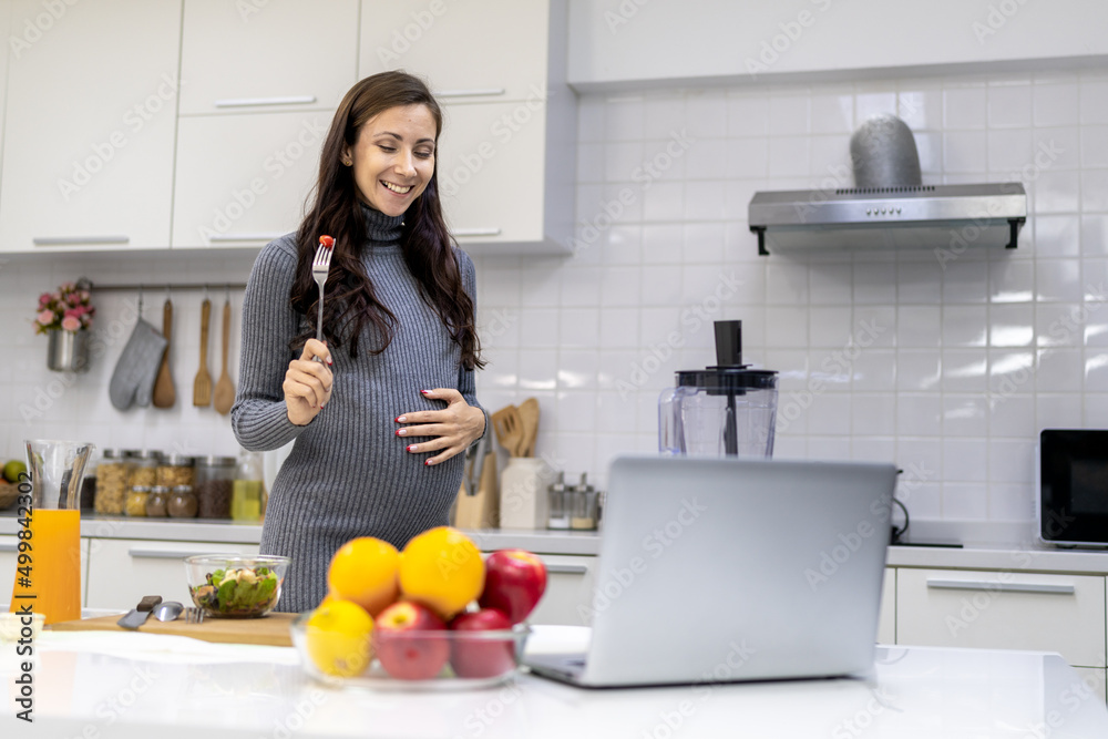 Wall mural healthy and cheerful pregnant woman preparing food for herself in her home kitchen. the menu is a ve