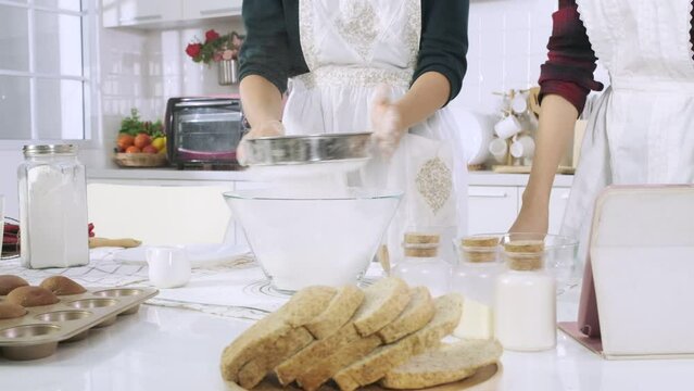 Woman sifting flour with sifter in the kitchen.