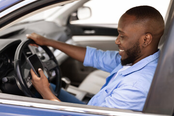 Happy black man using showing smartphone driving car