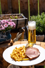 ready to eat - a grilled pork meat with fries on a white plate and a beer on the balcony at a sunny spring day