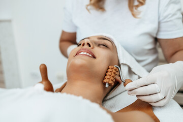 Fototapeta na wymiar Beautiful brunette getting face maderotherapy in a beauty salon. Professional skin care treatment.