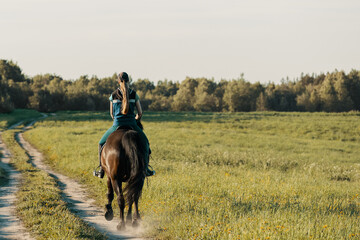 Teenage girl riding horse on country road, rear view.