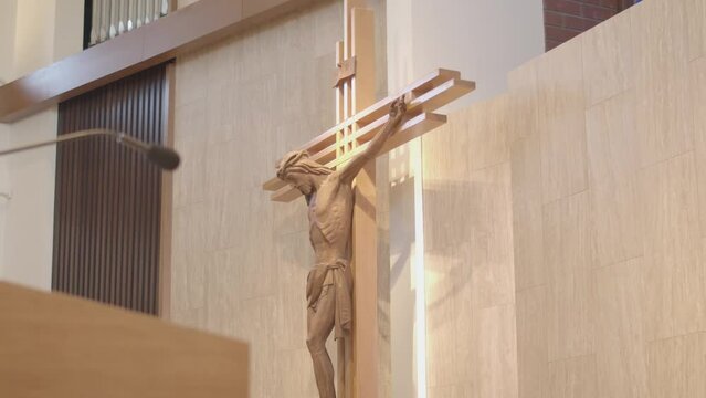 A dynamic footage of a church crucifix moving towards the left revealing a podium with a microphone. This footage is a representation of a cross with a figure of Jesus Christ crucified on it.