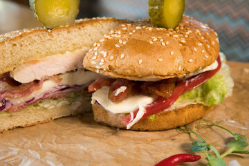 Burger with chicken breast, lettuce leaves, tomatoes, pickles and hot peppers