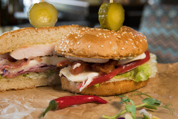 Burger with chicken breast, lettuce leaves, tomatoes, pickles and hot peppers