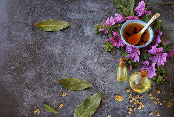 Hibiscus (Malva sylvestris) on the table with oil in a bottle and hibiscus tea in a cup .