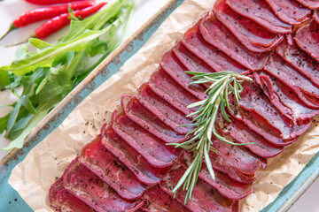 Basturma on a blue platter with cherry tomatoes, chili peppers and greens