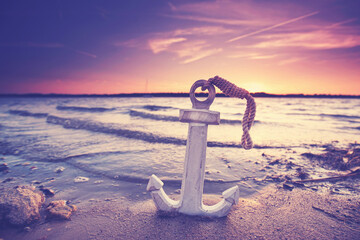 wooden anchor on romantic beach at sunset