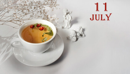 calendar date on light background with a porcelain cup of green tea, white gypsophila and angels with copy space. July 11 is the eleventh  day of the month