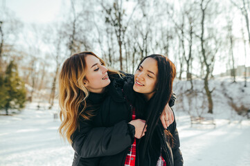 Happy two women spend time together in a snowy park while walking, hugging and smiling on a winter walk.