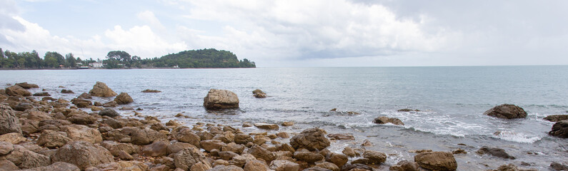 Beach with many rocks, beautiful sea with sky and gray background with light waves, suitable for relaxing, traveling, holiday without crowds.