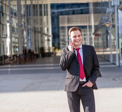 Smiling businessman wearing business suit talking on mobile phone.Modern office building background.Professional male worker wearing office uniform talking on cell phone.