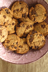 Pink plate filled with chocolate chip cookies on wooden table. Flat lay.