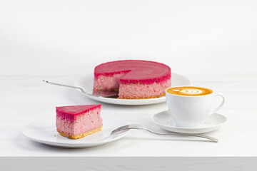 Homemade raspberry and strawberry cheesecake and cup of coffee cappuccino on white wooden table. Shallow focus.