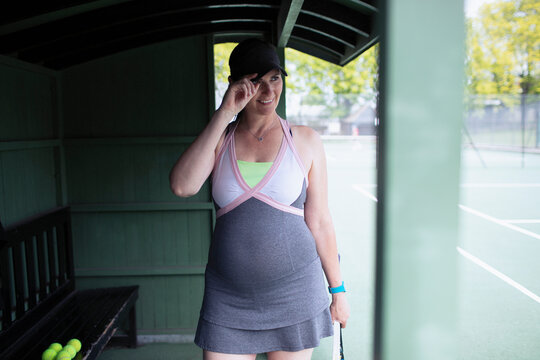Smiling pregnant woman in dress on tennis court