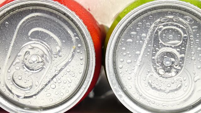 Water droplets from melting ice drip down the aluminum cans with beverages lying in the ice