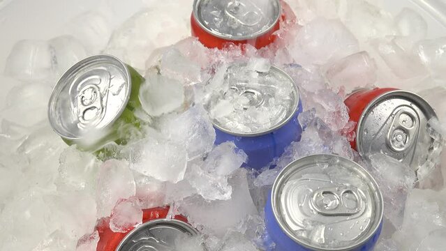 Pieces of ice are falling down on the aluminum cans with beverages lying in the ice