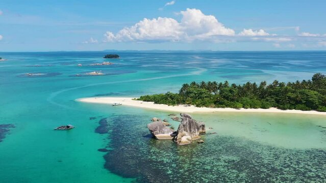 Aerial landscape panning shot of beautiful tropical islands and turquoise blue ocean on a sunny day in Indonesia with coral reefs and white sand beaches filled with coconut trees