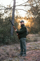 Man looking at camera and smiling while holding shotgun during hunting.