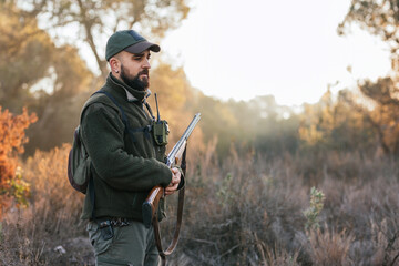 Adult man holding his gun in middle of nature looking down