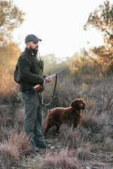 Young hunter standing and holding his shotgun in nature with his dog