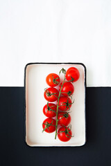 Fresh red cherry tomatoes on a branch, on a black and white background, top view. Creative food design. Minimalist layout.