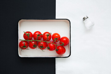 Fresh red cherry tomatoes on a branch, on a black and white background, top view. Creative food design. Minimalist layout.