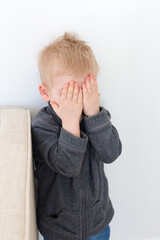 Three-year old blond boy hiding his eyes during a game of hide-and-seek