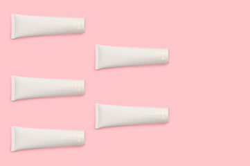White cosmetic bottles on a pink background. Cream for body care.