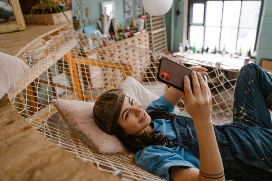 Young woman artist using cellphone while resting in hammock