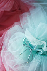 Tulle fabric mesh scattered in a chaotic manner. The background is a composition of blue and pink dresses for little girls with a lace in the form of a bow.