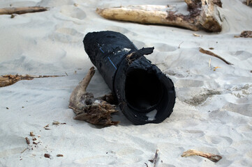 Zanieczyszczona plaża wyrzucone na brzeg odpady plastikowe duża gumowa rura plastikowy przewód 
