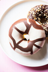 Two doughnuts with chocolate glaze and peanuts on a pink background. Close up.