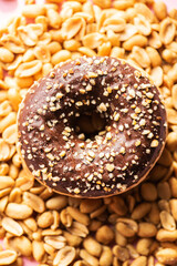 Doughnut with chocolate glaze and peanuts on a pink background. Top view.