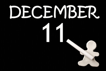 A small white plasticine man writing the date 11 December on a black board. Business concept. Education concept.
