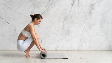 Banner of woman rolling her mat with both hands on after yoga class with copy space on the wall